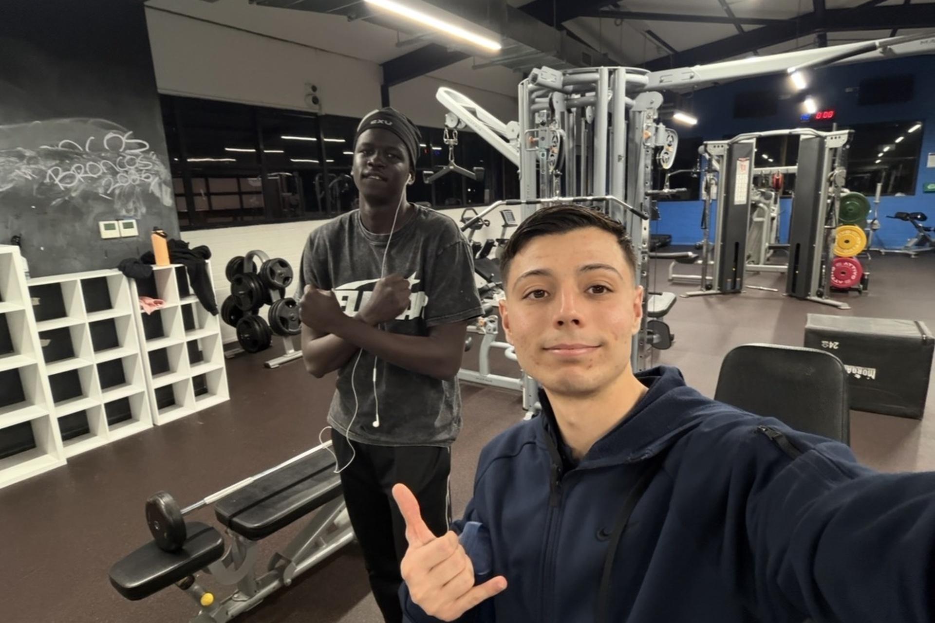 Two young men at the gym, one giving a thumbs up.
