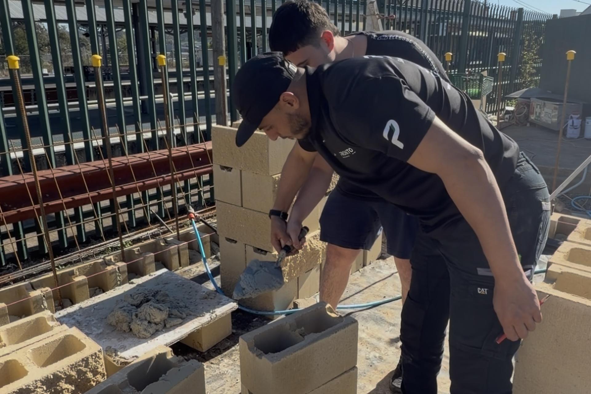 Two workers laying besser blocks together on an outdoor building site.