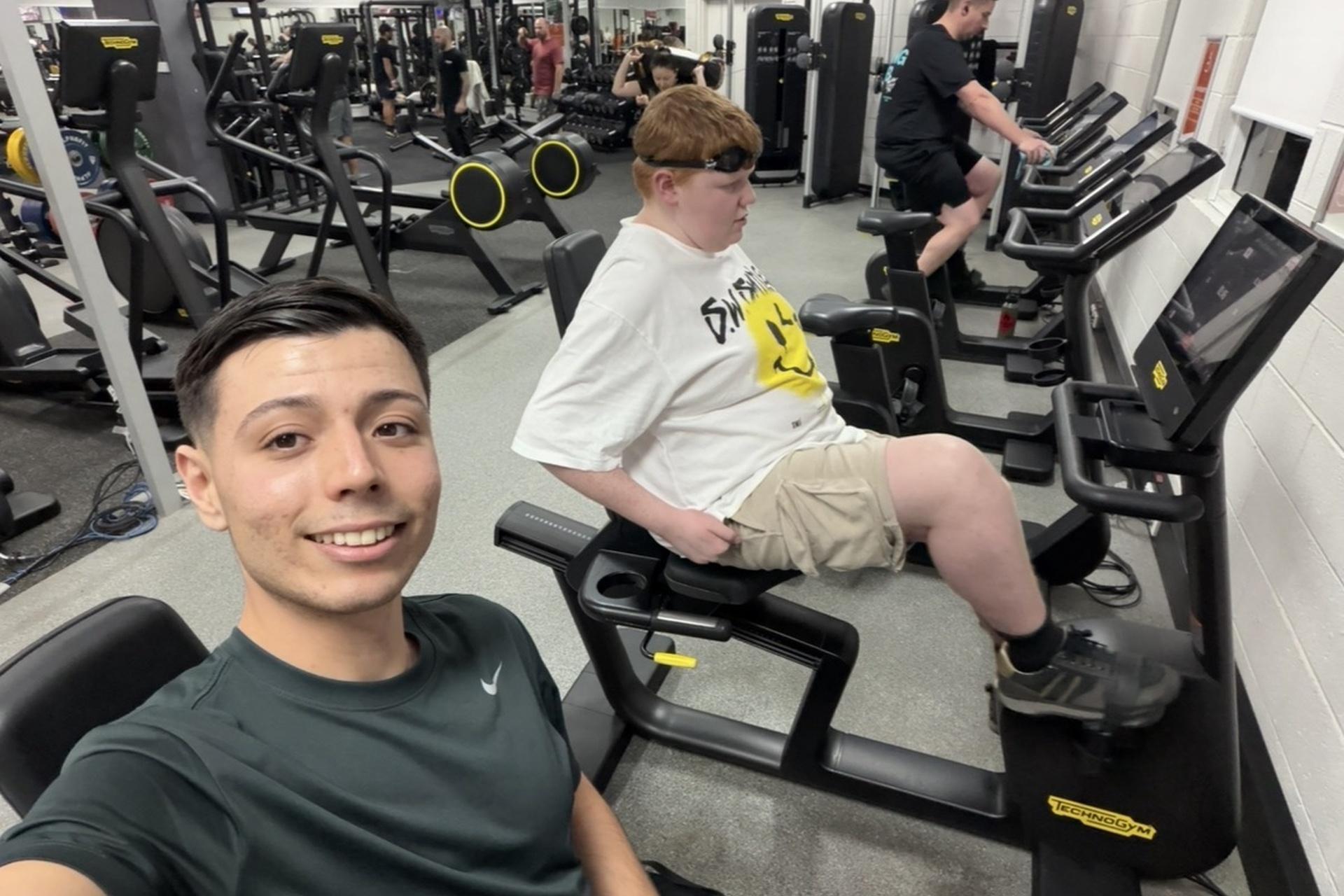 Two people at the gym, seated at the exercise bikes.
